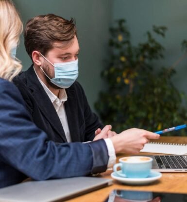 Two professionals wearing masks reviewing LCA status updates on a laptop during an H-1B visa application process.