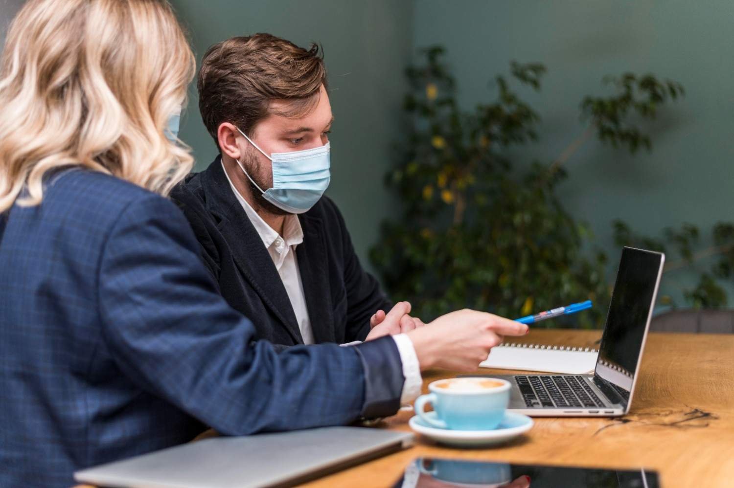 Two professionals wearing masks reviewing LCA status updates on a laptop during an H-1B visa application process.