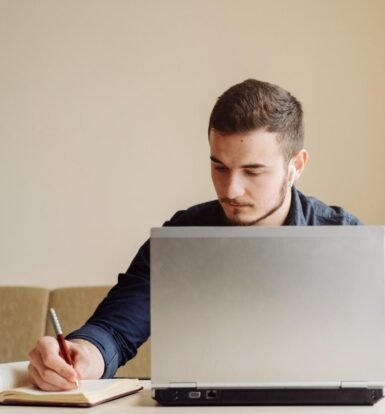 Man working on a laptop while taking notes, representing virtual paralegal support for USCIS Request for Evidence responses.