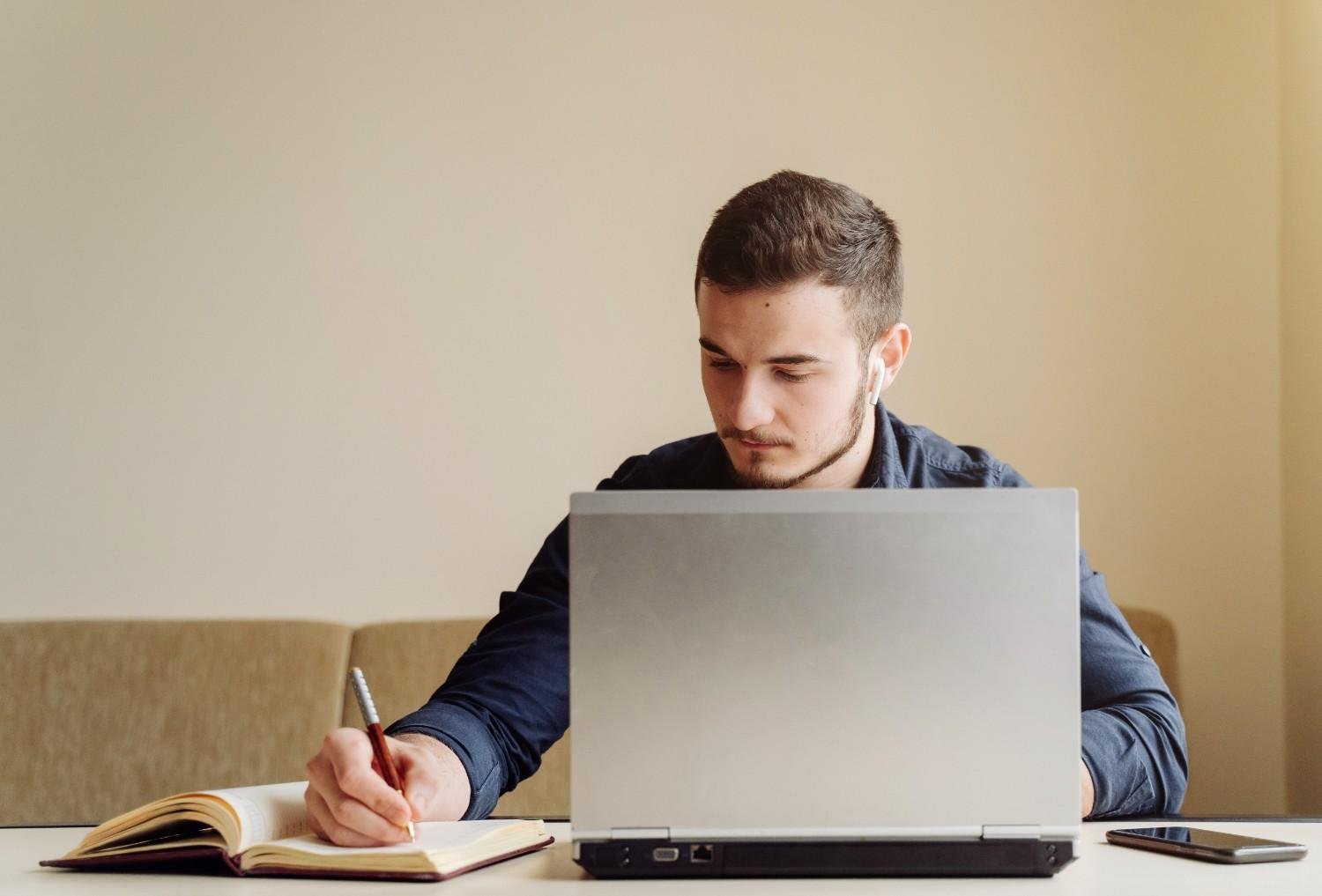 Man working on a laptop while taking notes, representing virtual paralegal support for USCIS Request for Evidence responses.