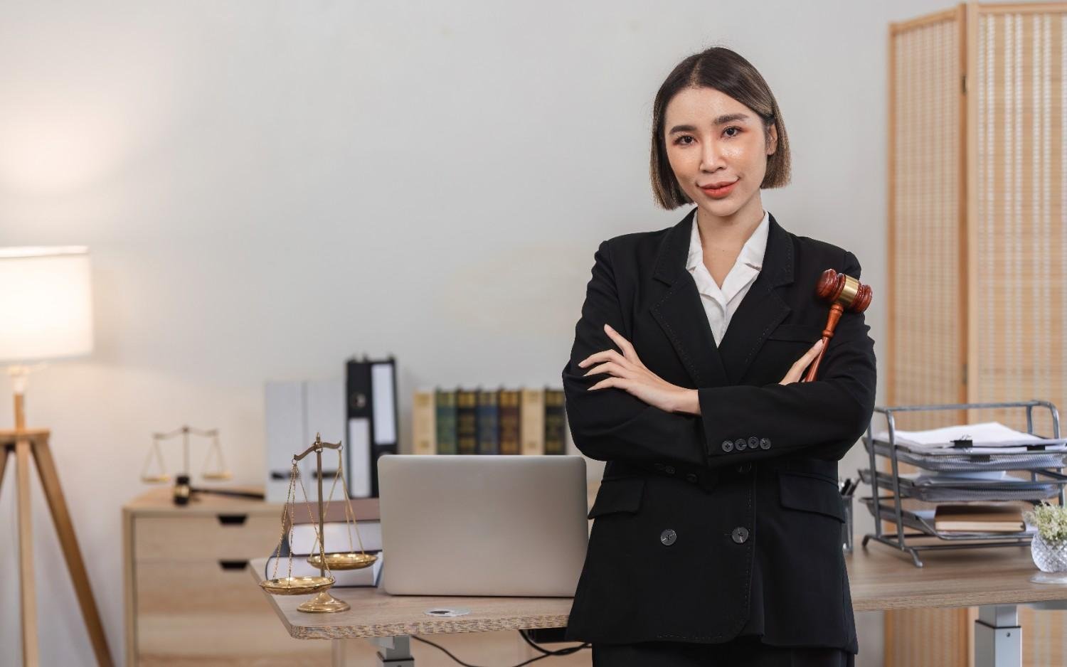 Confident female attorney in a law office, holding a gavel, with legal books, scales, and a laptop on the desk—illustrating the efficiency and professionalism gained from Virtual Legal Assistant Benefits for Small Law Firms.